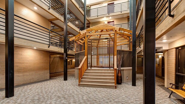 Un interior con varios niveles, una escalera de madera central, barandas de metal y una alfombra estampada.