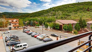 Un estacionamiento con varios autos, un edificio con techo rojo y un paisaje montañoso al fondo.