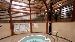 Un spa interior con una bañera de hidromasaje hexagonal, vigas de madera y varios letreros de precaución en las paredes.