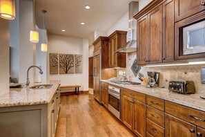 A kitchen with wooden cabinets, stainless steel appliances, a granite countertop, pendant lighting, and a tree-themed wall art piece. - Stunning ski-in/ski-out penthouse w/ shared pool, hot tub, sauna & gym (Park City)