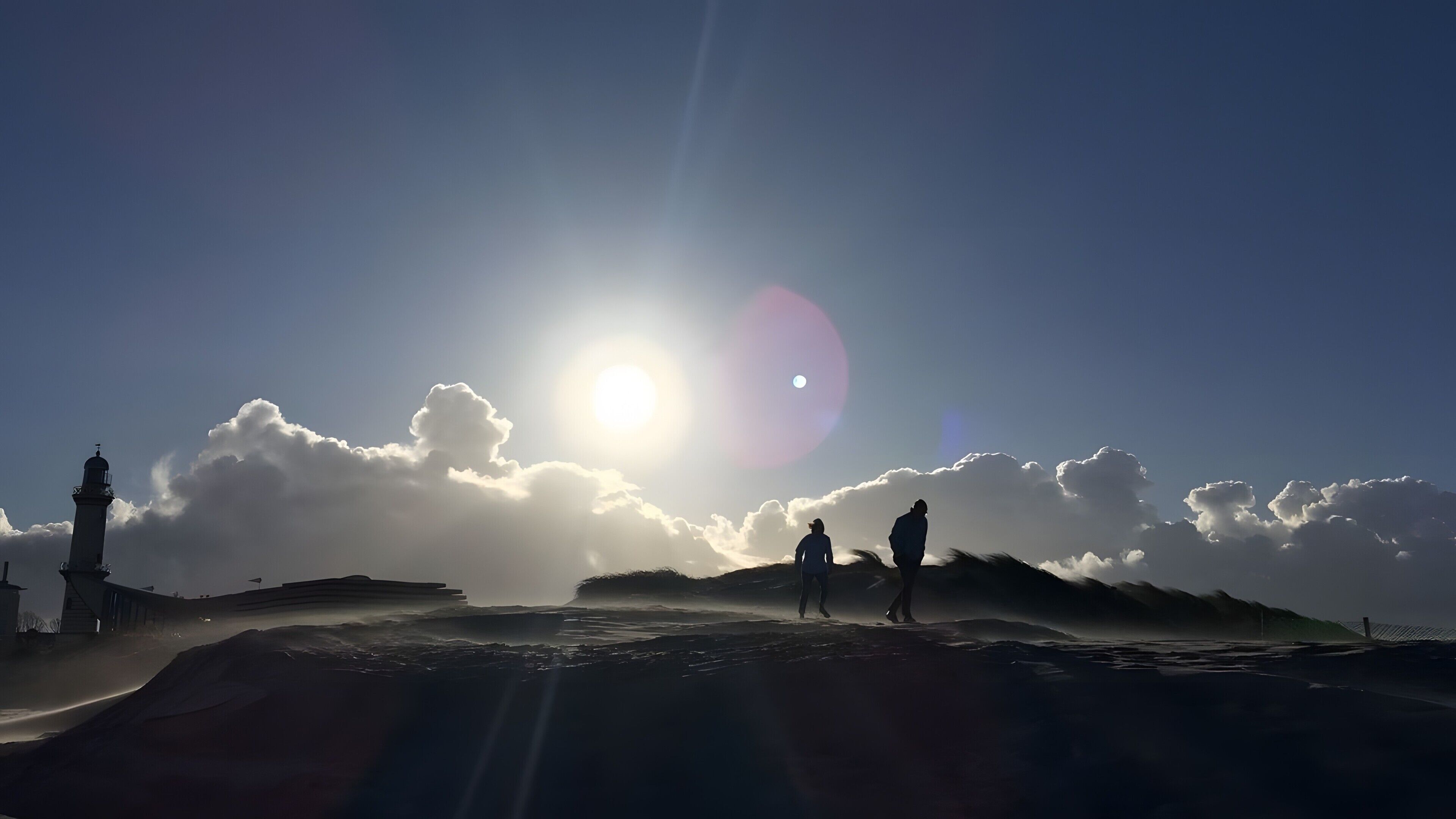A lighthouse silhouette, a person, and a sun with clouds in the sky.
