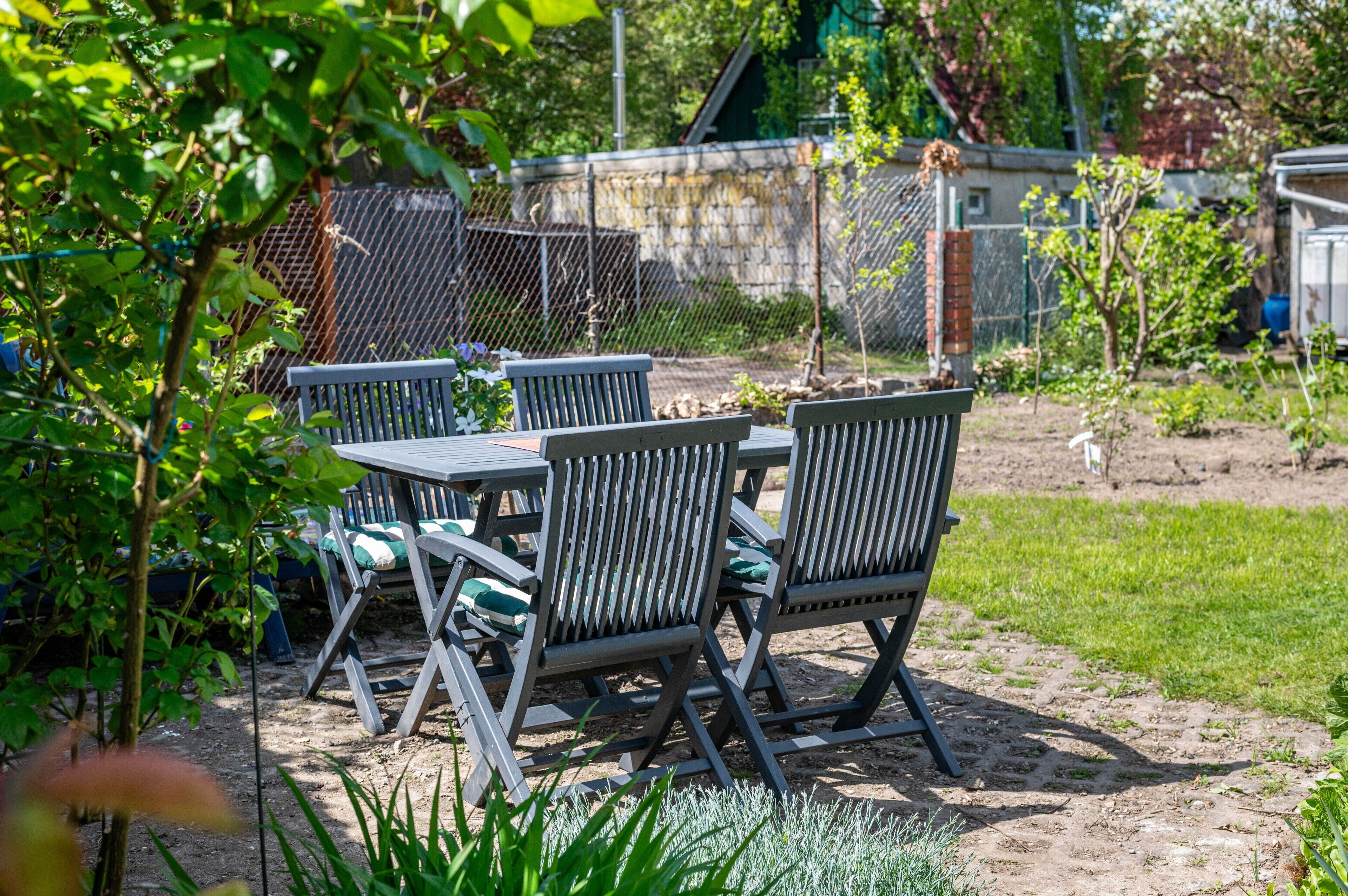 A garden with a table and chairs, surrounded by greenery and a fence.