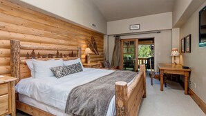 Ein schlafzimmer im Blockhausstil mit einem hölzernen Bett, einem Nachttisch, einem Schreibtisch und einem Fenster mit Vorhängen.