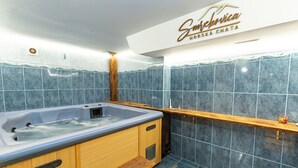 Een spa-ruimte met een jacuzzi, houten banken en een betegelde muur met een logo.