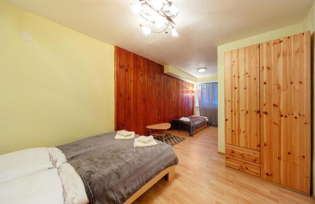 A bedroom with a bed, a small table, a wardrobe, and a wooden wall panel.