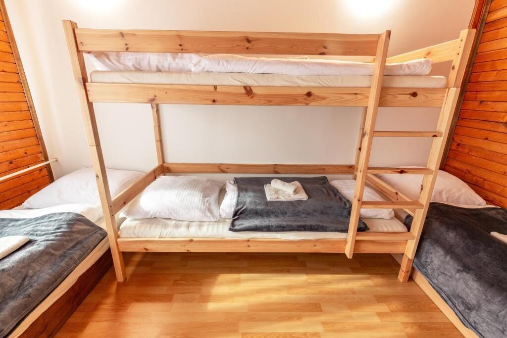 Habitación con literas, paredes y pisos de madera, una manta gris en la litera inferior y un almohadón blanco en la superior.