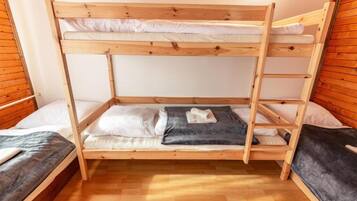Habitación con literas, paredes y pisos de madera, una manta gris en la litera inferior y un almohadón blanco en la superior.