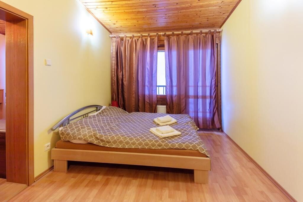 Een slaapkamer met een houten plafond, een bed met een bedsprei met een patroon, en een raam met gordijnen.