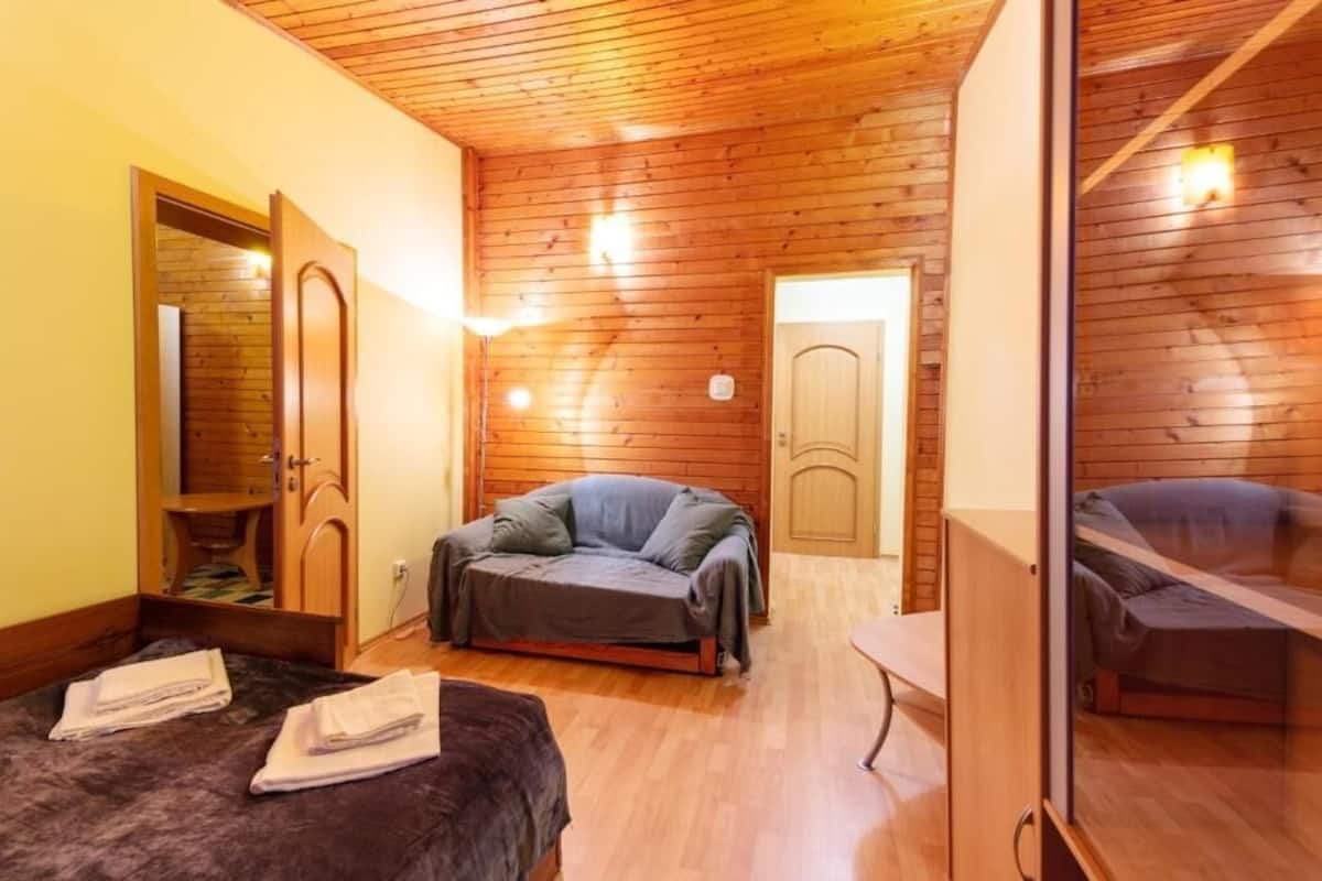 A room with wooden walls, a sofa, a bed, and a mirror.