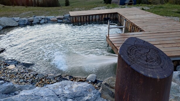 Een houten steiger die zich uitstrekt over een rivier, omringd door rotsen en kiezelstenen.