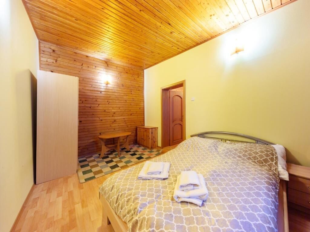 Un dormitori amb sostre de fusta, un llit amb un estovat estampat, una taula de fusta petita i una porta.