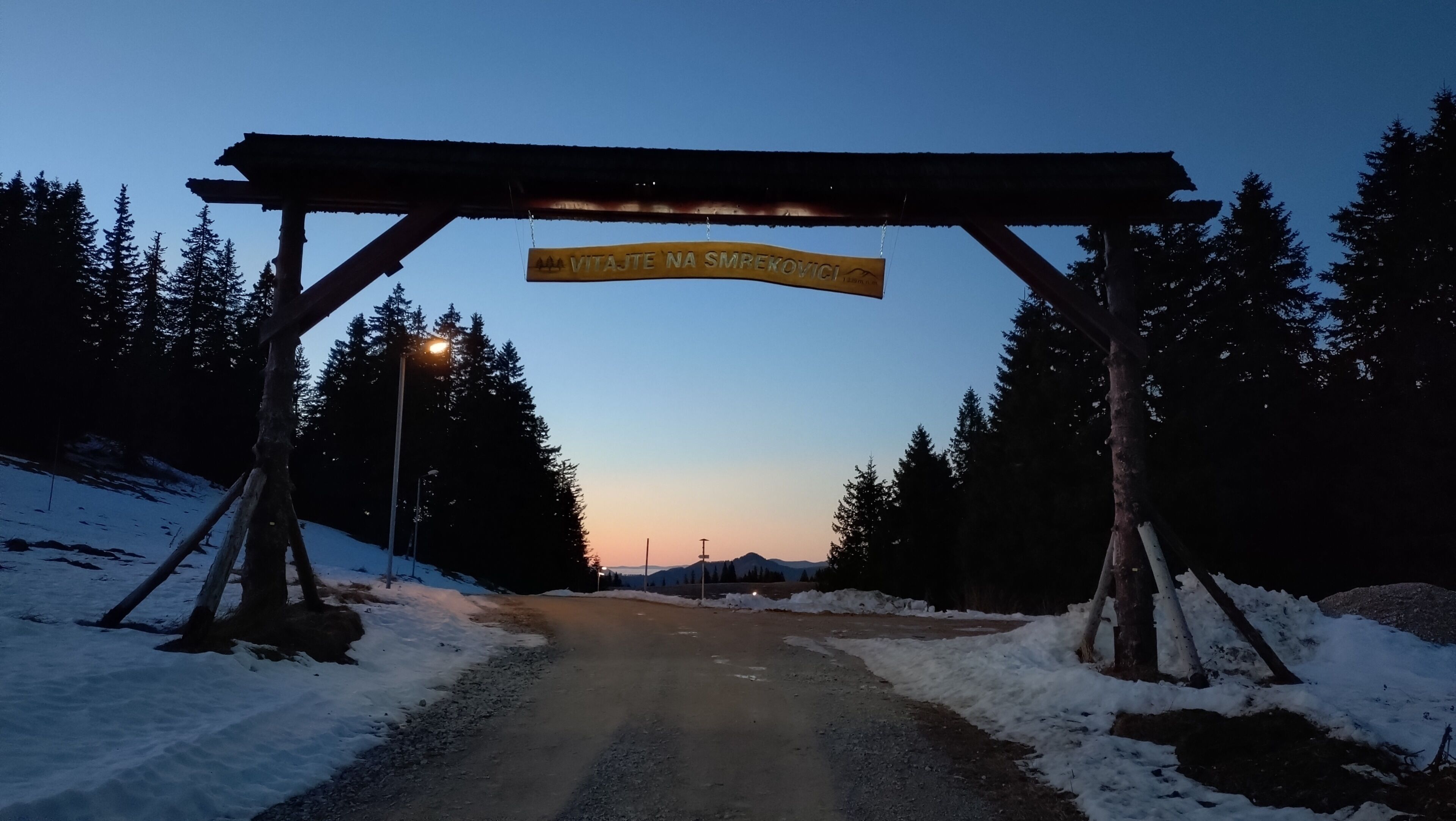 Una carretera nevada que conduce a un arco de madera con un letrero.