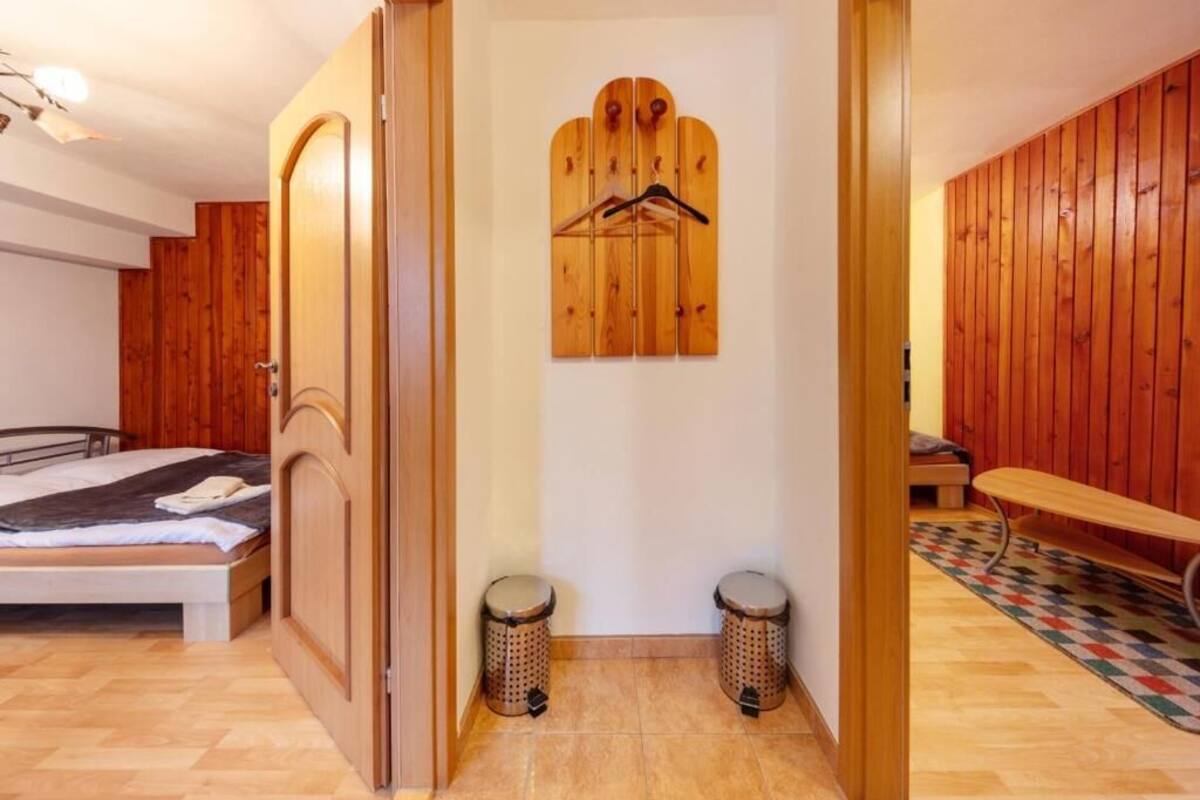 A bedroom with a bed, wooden wardrobe, a wooden coat rack, two trash bins, and a bench.