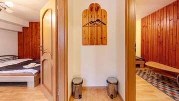 A bedroom with a bed, wooden wardrobe, a wooden coat rack, two trash bins, and a bench.