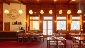 Een restaurant met houten inrichting, verschillende tafels en hangende lampen.