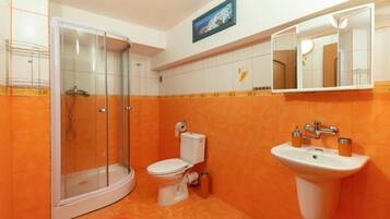 Un baño con cabina de ducha de vidrio, inodoro y lavamanos con espejo.
