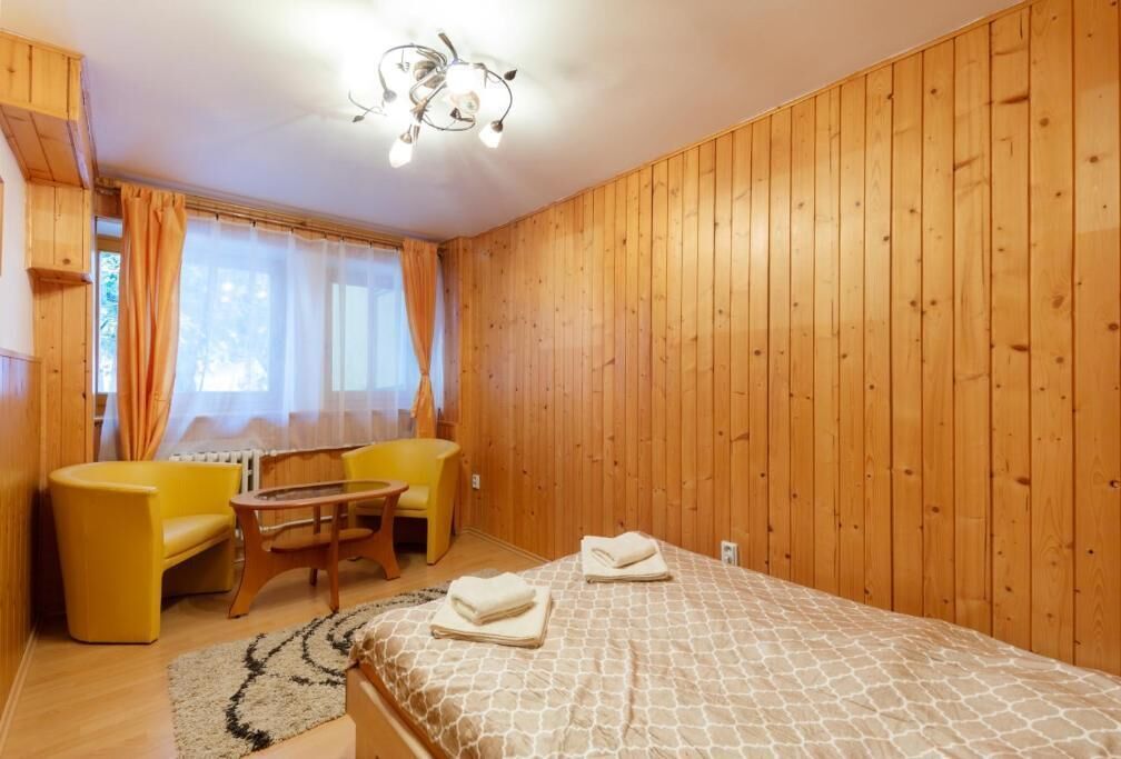 Ein Zimmer mit Holzwänden, einem Bett mit gemustertem Überwurf, einem gelben Sessel, einem Holztisch und einer Chandelier.