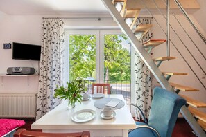 Une pièce comprenant une table à manger dressée pour deux personnes, un téléviseur fixé au mur et un escalier menant à un espace extérieur.