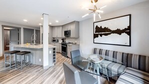 Una cocina moderna con una isla central, un área de comedor con mesa de vidrio y una sala de estar con sofá y una obra de arte colgada en la pared.