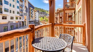 Ein Balkon mit Tisch und Stühlen, der auf einen Wohnbereich mit mehrstöckigen Gebäuden und eine hügelige Landschaft blickt.