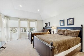 A bedroom with two beds, a large window with curtains, a bedside table with a lamp, and framed pictures on the wall. - Large & Luxurious Home with  Private Hot Tub, and Fireplace (Cottonwood Heights)