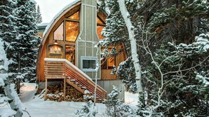 A cabin with a wooden exterior, a staircase, and a log pile outside.