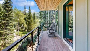 A wooden deck with a railing, a bench, and a door leading to a room.