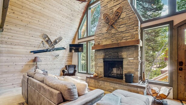 A cozy living room with a stone fireplace, leather sofas, and large windows.