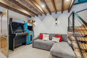 Un salon confortable avec un canapé, des jeux d’arcade et un escalier.