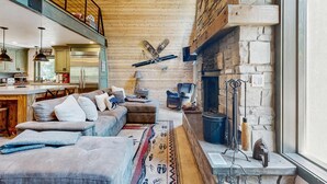 A spacious living area with a stone fireplace, a high ceiling, and a cozy seating arrangement.