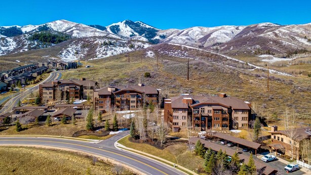 A multi-story hotel with a parking lot, surrounded by mountains and a clear sky. - Spacious mountain-view condo with fireplace, shared pool, hot tub & fitness room (Park City)