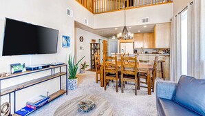 A spacious living area with a TV, wooden furniture, a dining table, and a kitchen in the background. - Spacious mountain-view condo with fireplace, shared pool, hot tub & fitness room (Park City)