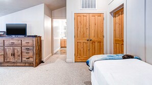A bedroom with a bed, a wooden dresser, a television on the dresser, and a closet with two doors. - Spacious mountain-view condo with fireplace, shared pool, hot tub & fitness room (Park City)