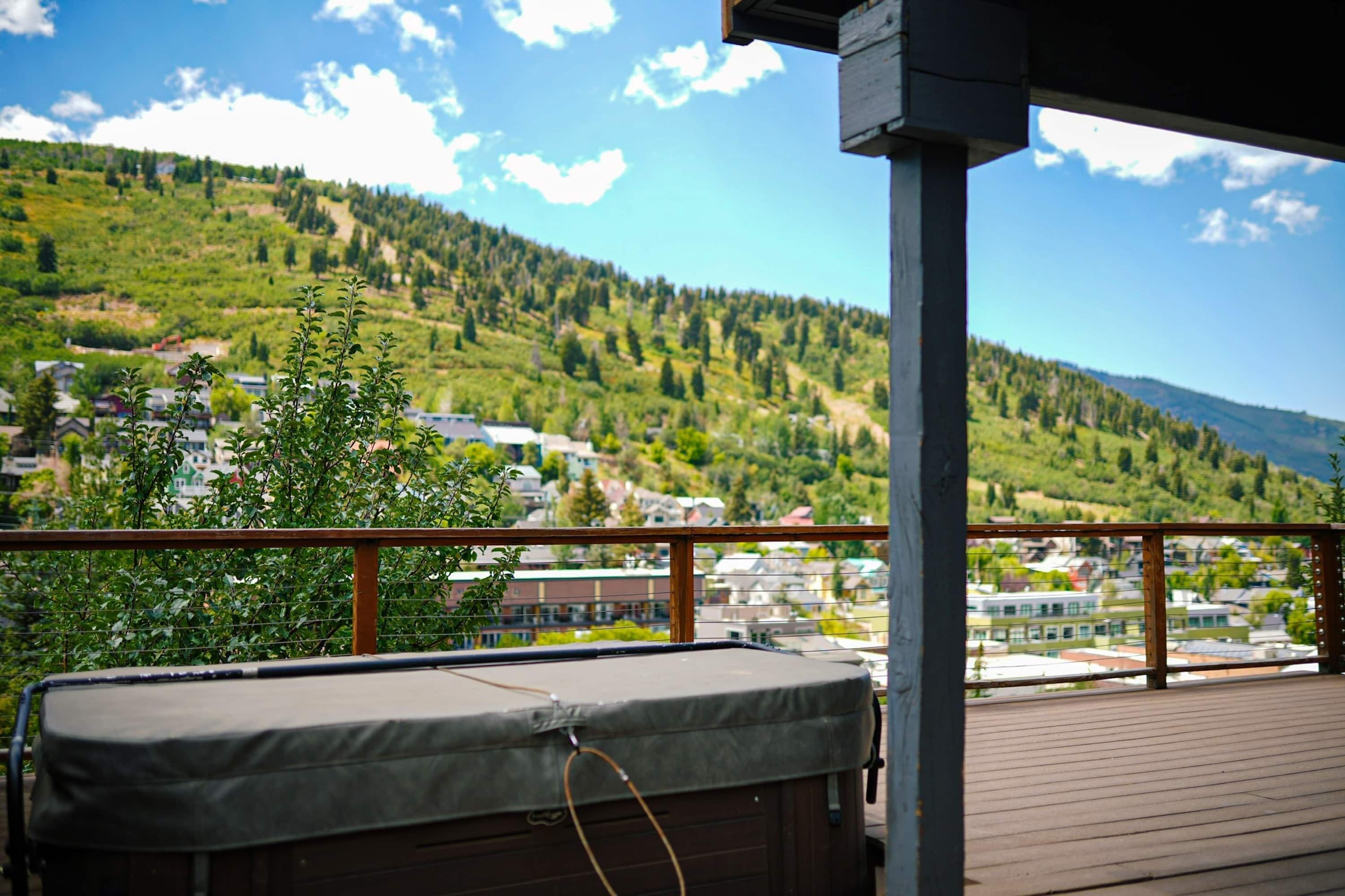 A wooden deck with a hot tub, overlooking a town and green hills.
