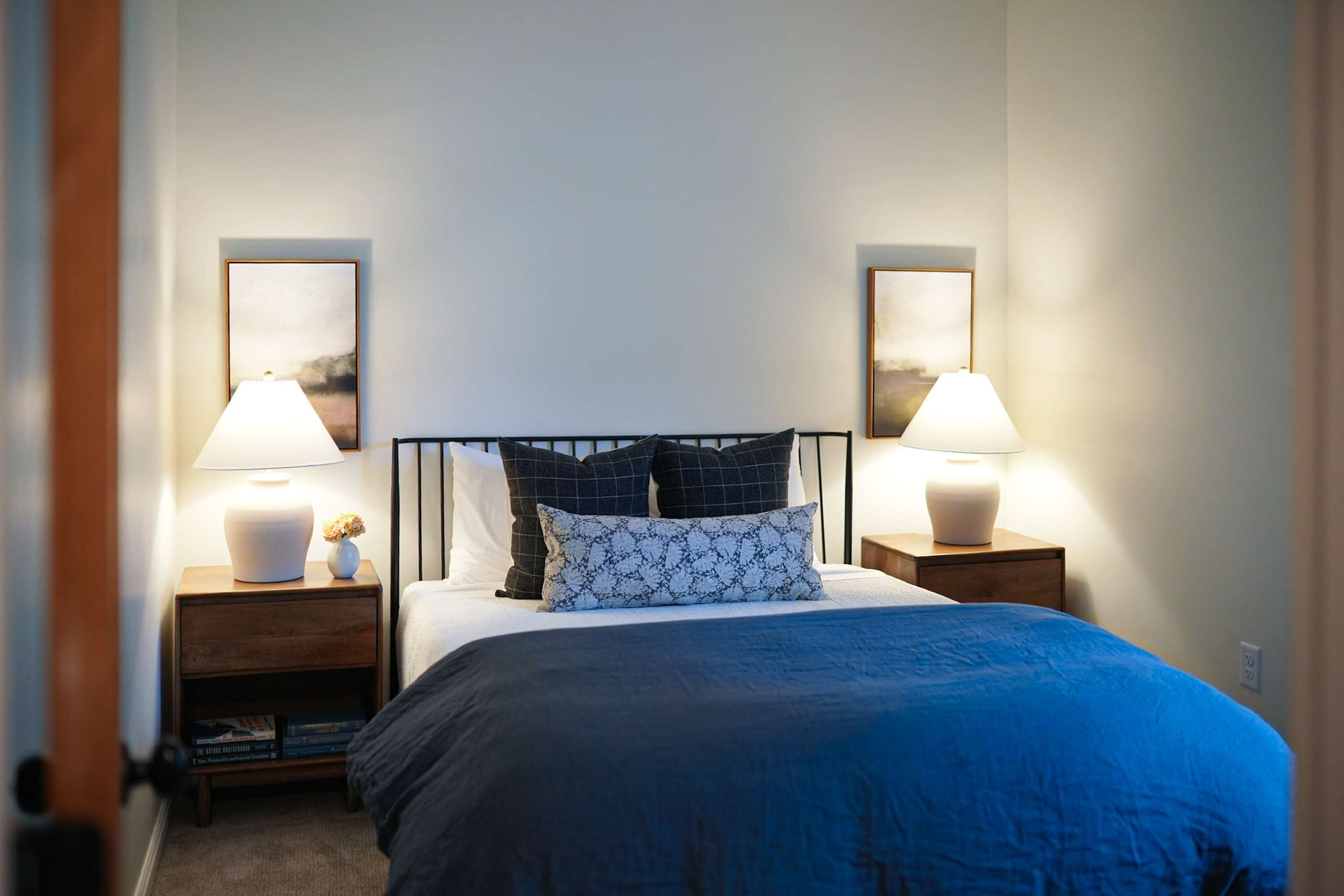 Une chambre à coucher avec un lit, deux tables de chevet avec des lampes, une commode et deux tableaux encadrés accrochés au mur.