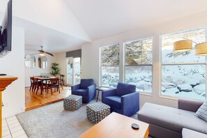Moderni olohuone, jossa on ruokailutila, suuret ikkunat, joista avautuu lumipeitteinen maisema, sekä kattotuuletin.
