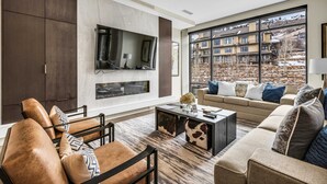 Una sala de estar moderna con chimenea, ventanas amplias y vistas a un conjunto de edificios.
