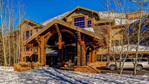 Una cabaña con una entrada de madera grande, un tejado cubierto de nieve y un cartel que dice 'The Lodges at Deer Valley'.