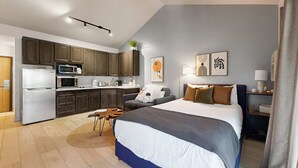 Ein modernes Hotelzimmer mit einem großen Bett, einer Küchenzeile, einem Essbereich und Bildern an den Wänden.