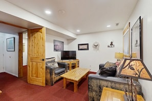 A living room with a wooden door, a television, a sofa, a coffee table, and wall decorations. - Spacious ski getaway with private hot tub & game room -Close to little and big Cottonwood Canyons (Sandy)