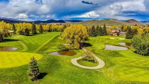 Un campo da golf con uno stagno, alberi e una catena montuosa in lontananza.
