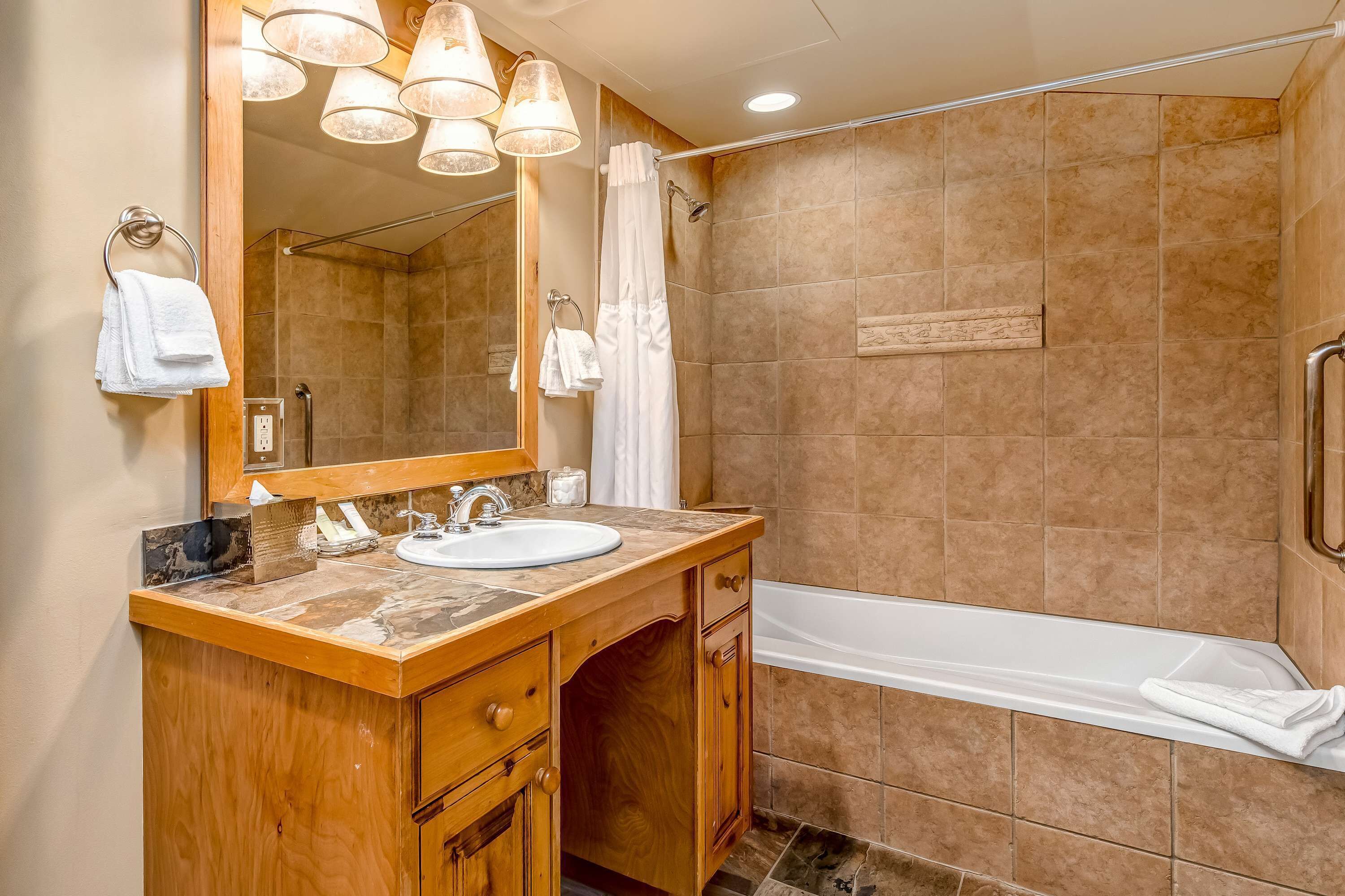 A bathroom with a wooden vanity, a sink, a mirror, a shower, and a bathtub.