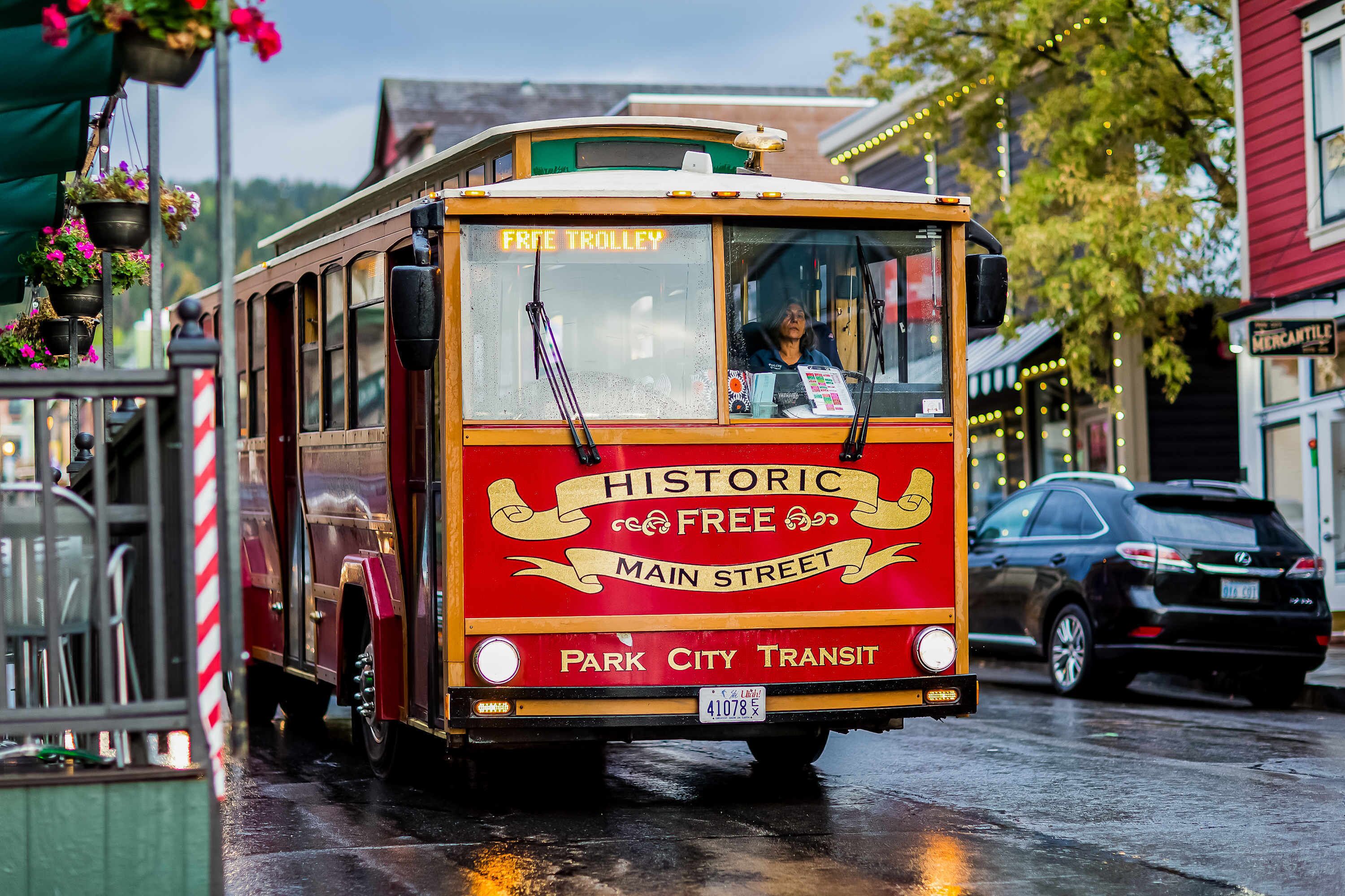 A historic free trolley with 'Historic Free Main Street' and 'Park City Transit' labels, driving on a wet street.