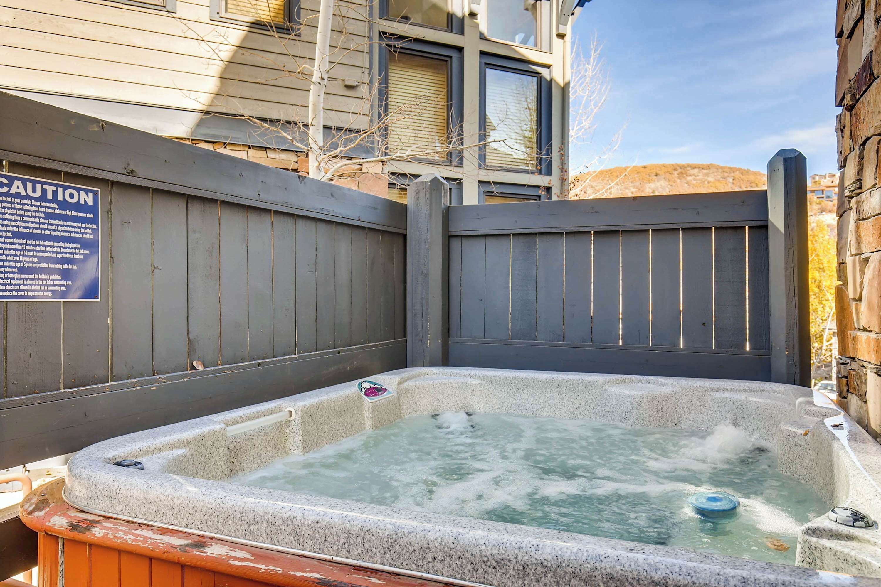 A hot tub with a wooden fence and a caution sign.