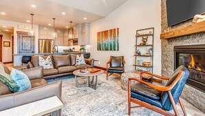A modern living room with a fireplace, leather sofas, a coffee table, and a kitchen in the background. - Stunning dog-friendly mountain condo with hot tub, gas grill, & AC (Kamas)