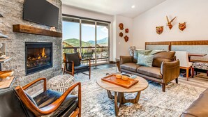 A spacious living room with a fireplace, leather furniture, a flat-screen TV, and a large window offering a mountain view. - Stunning dog-friendly mountain condo with hot tub, gas grill, & AC (Kamas)