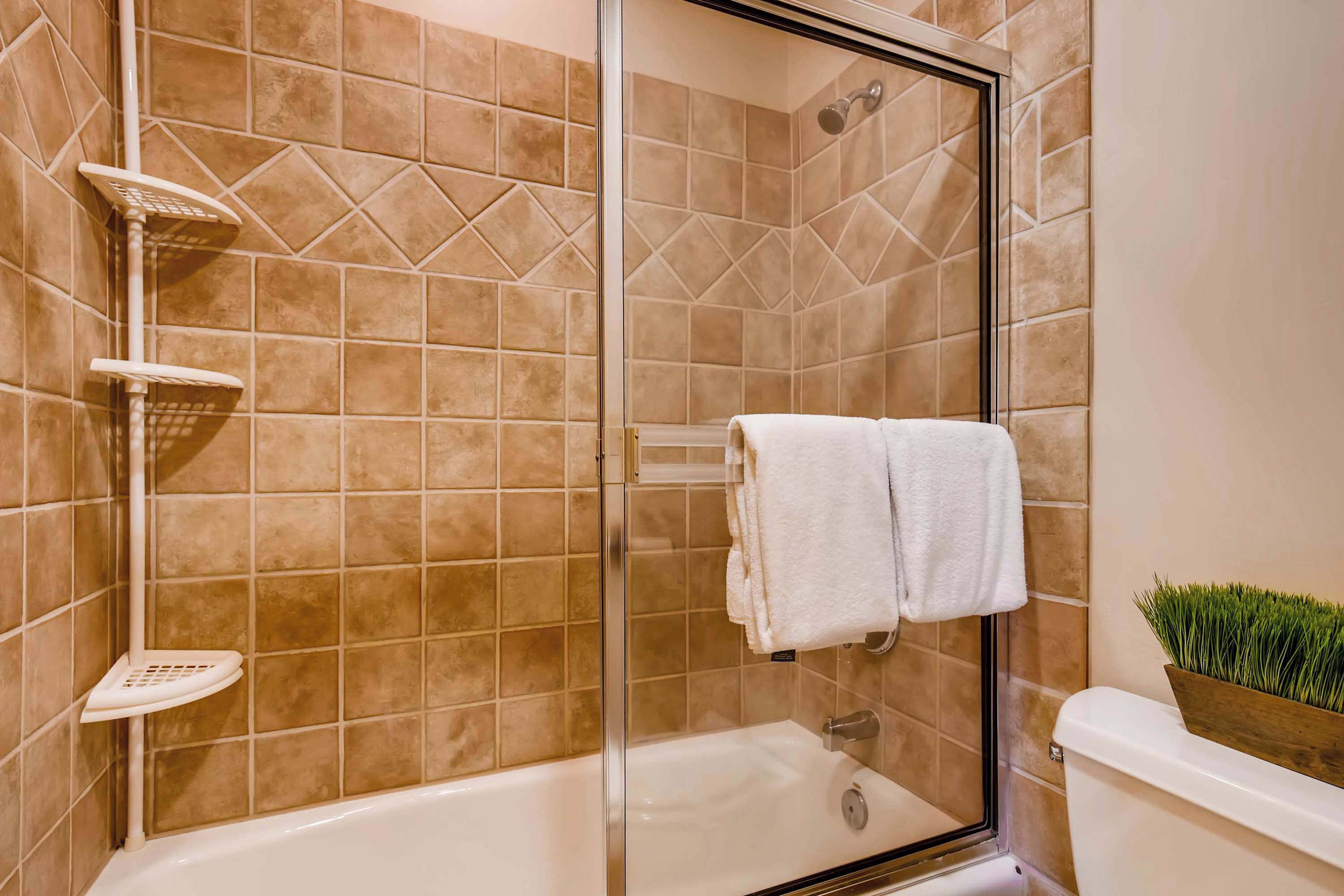 Une salle de bain avec une douche à parois de verre, une baignoire blanche et une serviette blanche accrochée au mur.