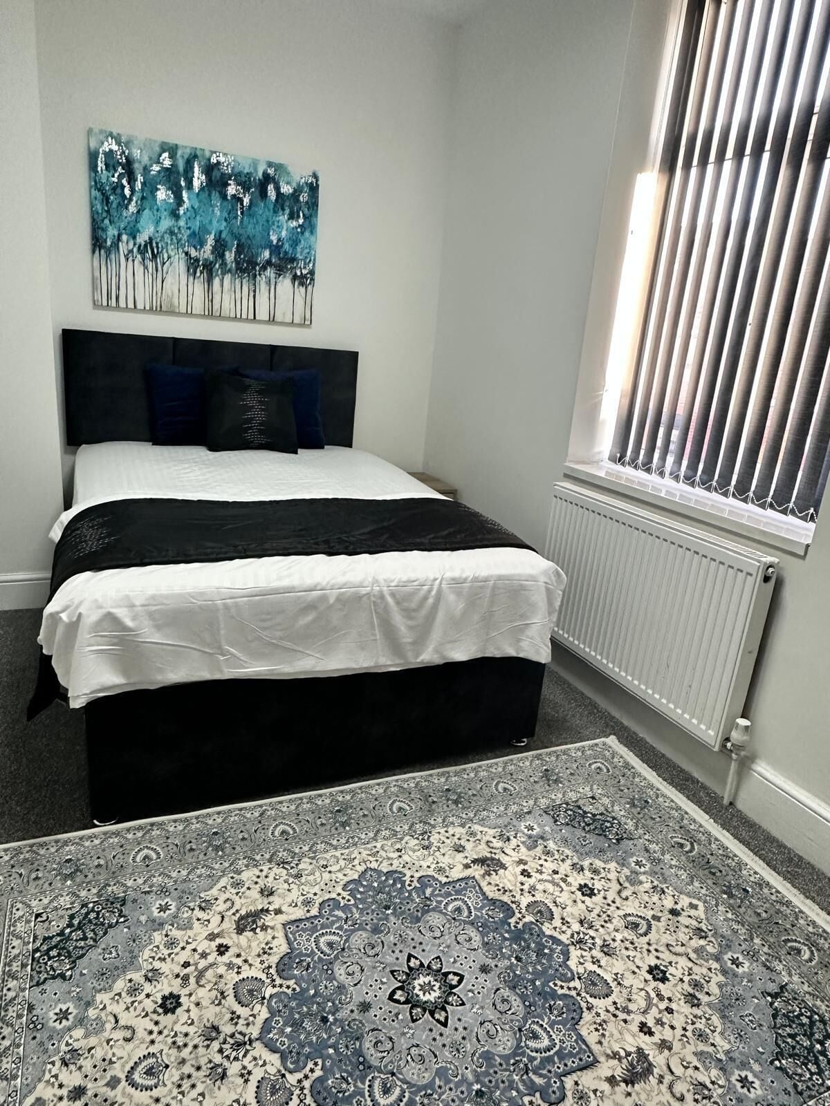 Un dormitorio con una cama, un radiador, una ventana con persianas y un tapete grande con estampado.