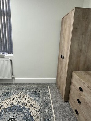 Ein Zimmer mit Heizkörper, Teppich mit Muster, Kleiderschrank und Schrank.
