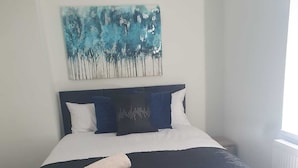 A neatly made bed with a blue and white bedspread, a rolled towel, and a blue and white pillow arrangement. - Modern 3bedroom Home in Bury Premium Mattresses Blackout Blinds Ensuite M (Bury)